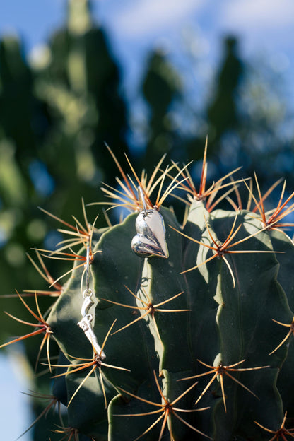 Close-up of a set of earrings, a heart and a pistol on half hoops, on a cactus with thorns against a blurred natural background